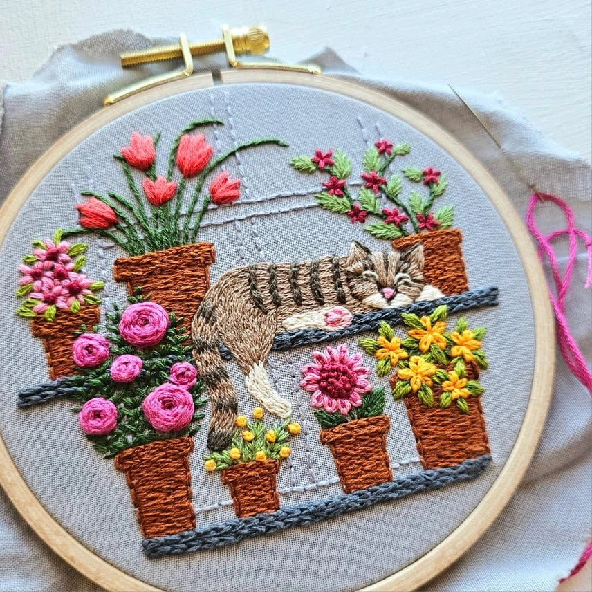 The 5 Cat Nap with Flowers Embroidery Kit by Jessica Long Embroidery features a gray tabby cat sleeping on a shelf amid colorful potted flowers—an adorable addition to any floral embroidery collection.